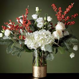 White flowers and red berry branches in a glass vase with a gold base
