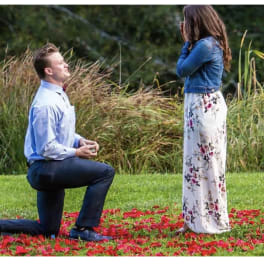 Man kneeling before woman standing on a flower petal-covered lawn