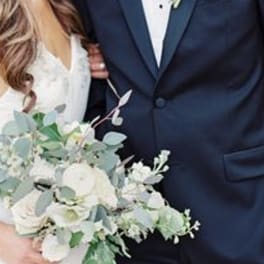 Bride holding a white and pale green bouquet beside a groom in a navy suit