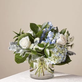 White roses and blue hydrangeas in a clear glass vase