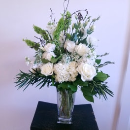 White floral arrangement in a clear glass vase with tall greenery