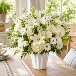 White floral arrangement in a white vase with lilies, roses, and daisies