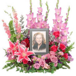 Standing floral tribute with a framed portrait and pink lilies, roses, and gladiolus