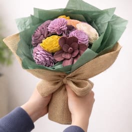 Handheld bouquet of multicolored flowers wrapped in burlap and green paper