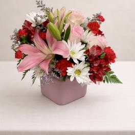 Pink lilies, roses, and daisies arranged in a pink square vase