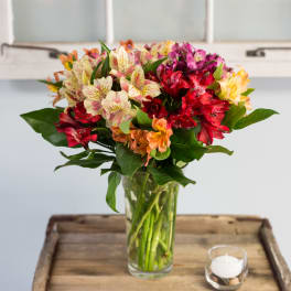 Mixed bouquet of alstroemeria in a glass vase beside a small candle