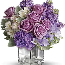 Purple roses and lavender flowers arranged in a clear square vase