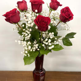 Red roses arranged in a burgundy vase with white baby's breath