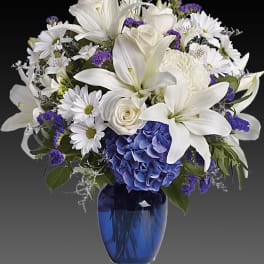 White lilies and daisies with blue hydrangea in a blue vase
