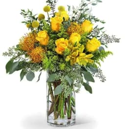 Yellow roses and mixed greenery arranged in a clear glass vase