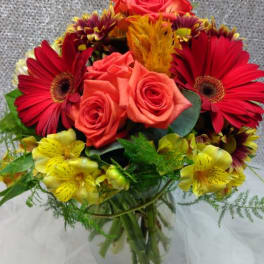 Bouquet of red gerbera daisies, coral roses, and yellow alstroemeria in a glass vase