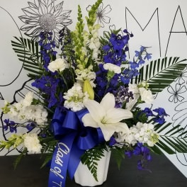 White and blue floral arrangement in a white vase with a blue ribbon