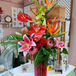 Tropical bouquet with red anthuriums, pink lilies, and orange bird-of-paradise in a red vase