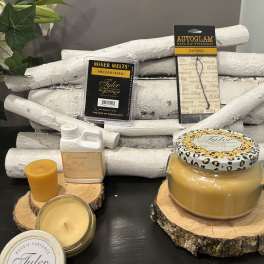 Assorted candles and fragrance products arranged on wood slices with white birch logs.