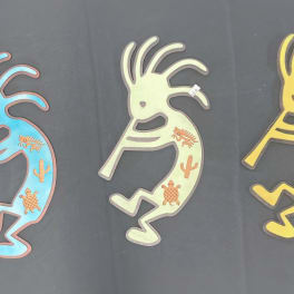Three colorful Kokopelli-style wall decorations on a dark background