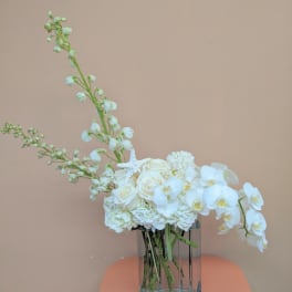 White floral arrangement in a clear glass vase with orchids and roses