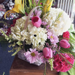 Basket arrangement with white hydrangeas, pink tulips, pink daisies, yellow lilies, and carnations.