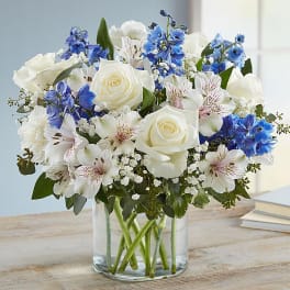 White roses and blue flowers arranged in a clear glass vase