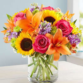Bouquet of sunflowers, orange lilies, and pink roses in a glass vase
