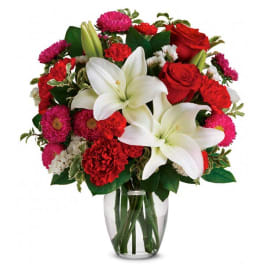 Bouquet of red and pink flowers with white lilies in a clear glass vase