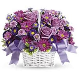 Purple flower arrangement in a white wicker basket with lavender ribbons