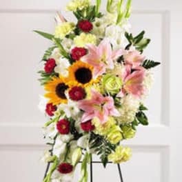 Standing spray with pink lilies, sunflowers, and mixed blooms on a metal easel.