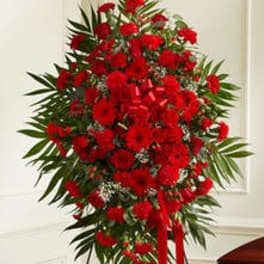 Standing spray of red carnations with palm fronds and red ribbon