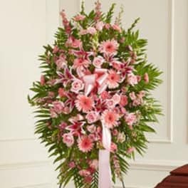 Standing pink funeral spray with roses, lilies, and gerbera daisies on a metal easel with ribbon.