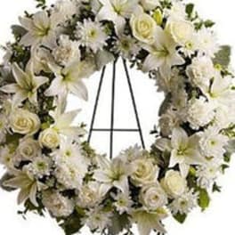 White floral wreath of lilies, roses, and mums displayed on a metal easel stand