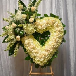Heart-shaped white floral wreath on a stand with green accents