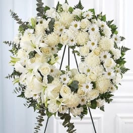 White floral wreath on a black easel with lilies, roses, and daisies