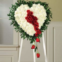 Heart-shaped floral wreath with white flowers and red roses on a stand