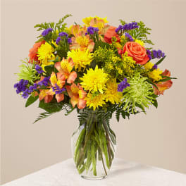 Mixed bouquet of yellow, orange, and purple flowers in a clear glass vase
