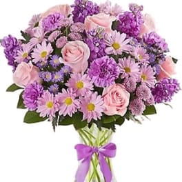 Pink and purple bouquet of roses and daisies in a glass vase with a ribbon