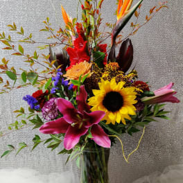 Tall mixed bouquet with sunflowers, lilies, and tropical blooms in a glass vase