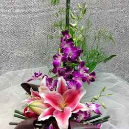 Asymmetrical pink lily and purple orchid arrangement with tall linear accents on sheer fabric