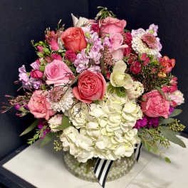 Pink and white rose bouquet in a clear glass vase with a striped ribbon