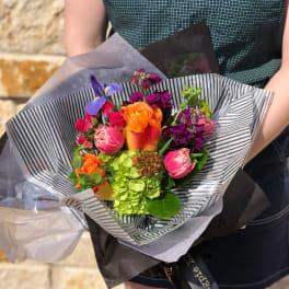 Handheld bouquet of orange, pink, purple, and green flowers wrapped in striped paper