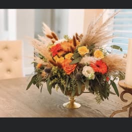 Orange and yellow flower arrangement in a gold pedestal bowl