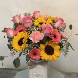 Pink roses and gerbera daisies with yellow sunflowers in a white vase