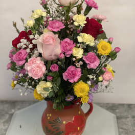 Mixed bouquet in a painted ceramic pitcher with pink, yellow, and red blooms
