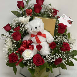 Red roses and white flowers arranged with a teddy bear and gift box