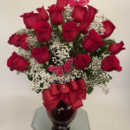 Red roses with baby's breath in a glass vase, accented by red bows and butterfly picks