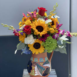 Bright mixed bouquet with sunflowers, roses, orchids, and butterflies in a painted vase