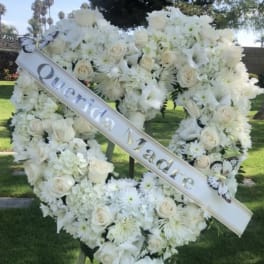White floral funeral wreath on an easel with a diagonal memorial ribbon