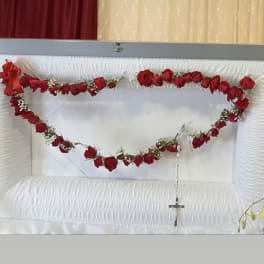 Red rose garland draped across a white casket with a cross pendant