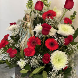 Red roses and gerbera daisies arranged around a small statue in a box.
