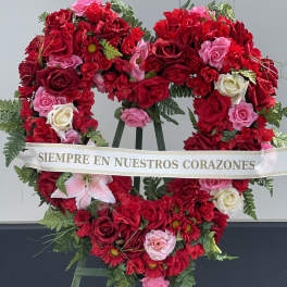 Heart-shaped floral wreath of red and pink roses with a memorial ribbon