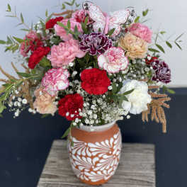 Mixed bouquet of carnations in a patterned vase with a butterfly decoration