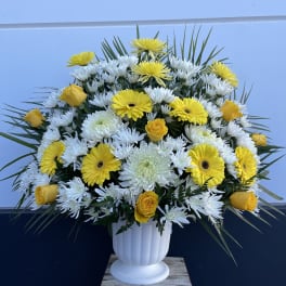 Yellow roses and white daisies in a white urn vase